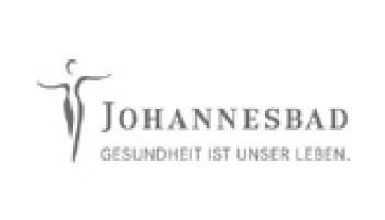 Das Logo zeigt eine stilisierte menschliche Figur mit erhobenen Armen in einer anmutigen Pose, neben dem Text „JOHANNESBAD“ in Großbuchstaben. Darunter steht in kleinerer Schrift „GESUNDHEIT IST UNSER LEBEN“, was übersetzt „Gesundheit ist unser Leben“ bedeutet.